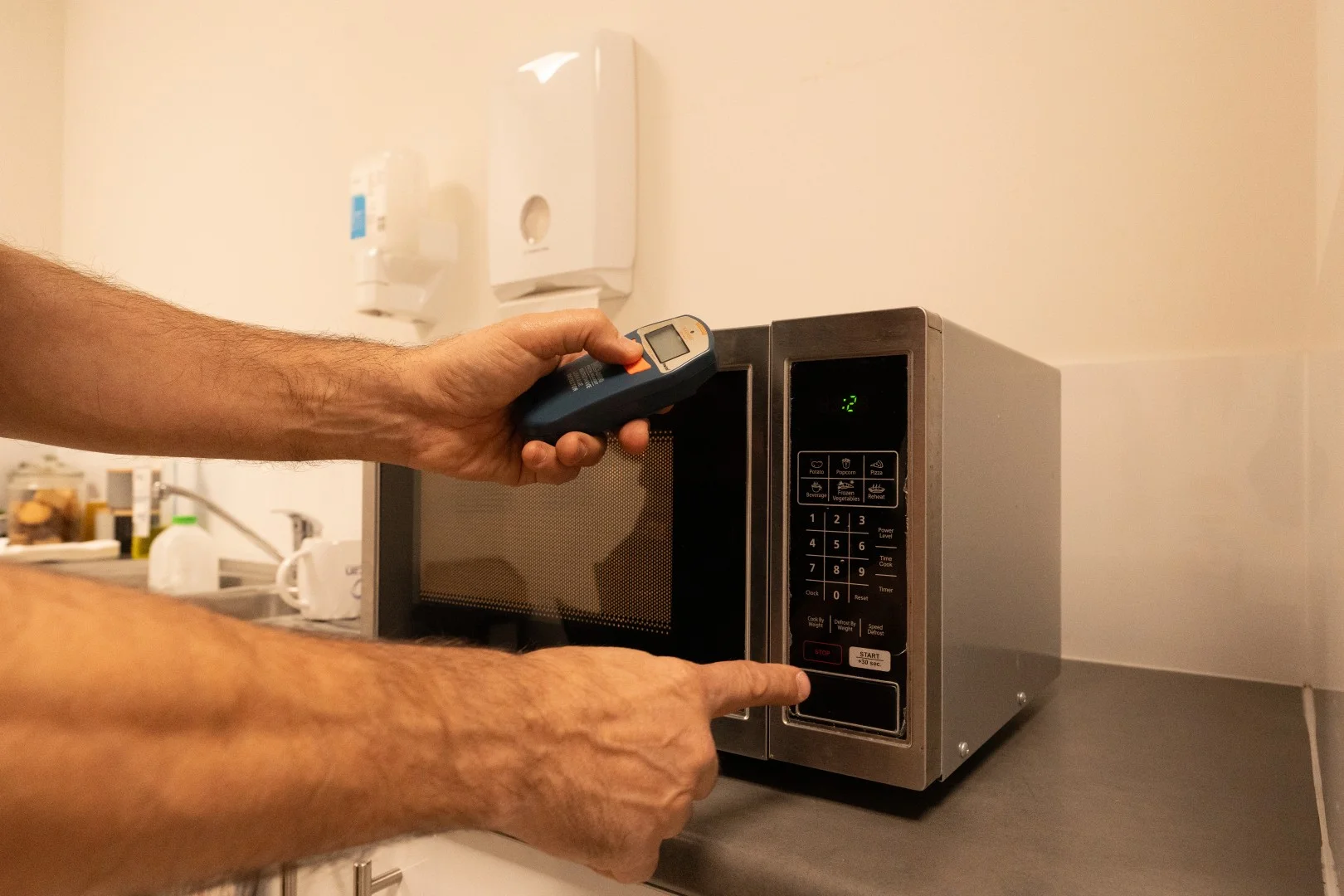Technician testing a microwave in a staff kitchen for leakage